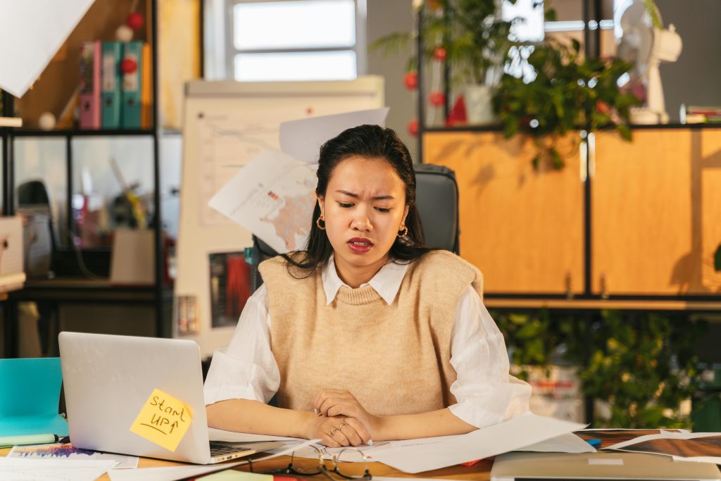 An office worker showing frustration while sitting at a cluttered desk with a laptop.