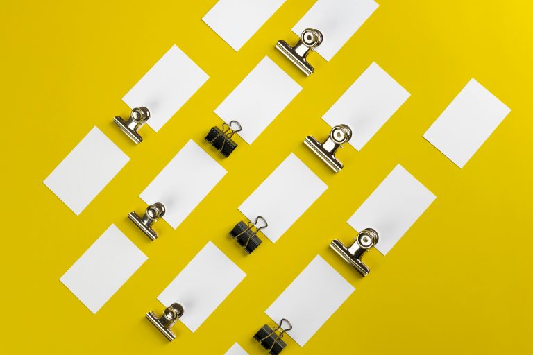 Top view of paper clips and blank cards arranged on a vivid yellow background.