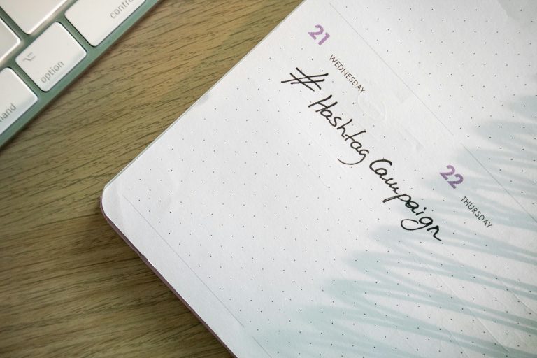 Open planner with 'Hashtag Campaign' handwritten next to keyboard. Ideal for social media and productivity themes.