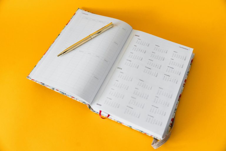 Open planner for 2023-2025 with a golden pen on a vibrant yellow background, perfect for organizing and planning.